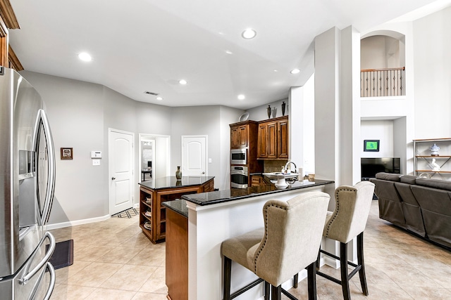 kitchen with appliances with stainless steel finishes, light tile patterned floors, kitchen peninsula, and a kitchen breakfast bar