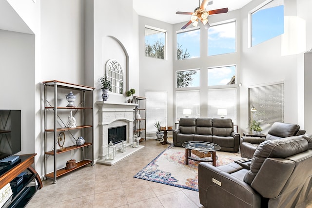 living room with light tile patterned floors, a towering ceiling, a high end fireplace, and ceiling fan