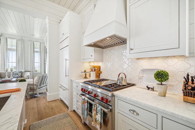 kitchen featuring custom exhaust hood, range with two ovens, light hardwood / wood-style flooring, light stone counters, and white cabinetry