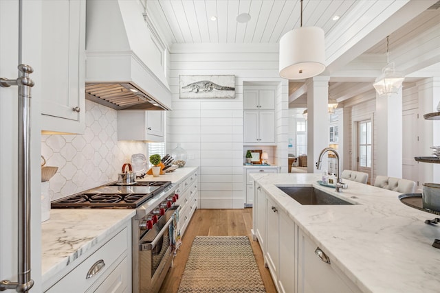 kitchen featuring pendant lighting, double oven range, premium range hood, sink, and light wood-type flooring