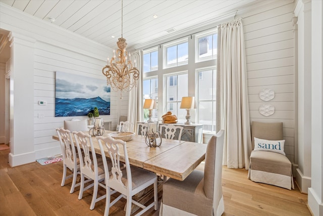 dining room featuring a chandelier, wooden walls, and light hardwood / wood-style flooring