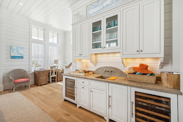 bar with white cabinets, light hardwood / wood-style floors, wood walls, and wine cooler