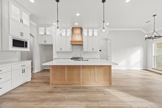 kitchen with white cabinets, a center island with sink, hanging light fixtures, and premium range hood