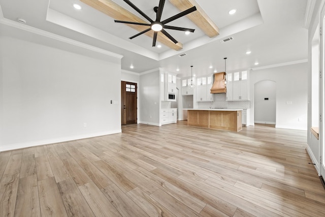 unfurnished living room with ornamental molding, light wood-type flooring, a tray ceiling, and ceiling fan