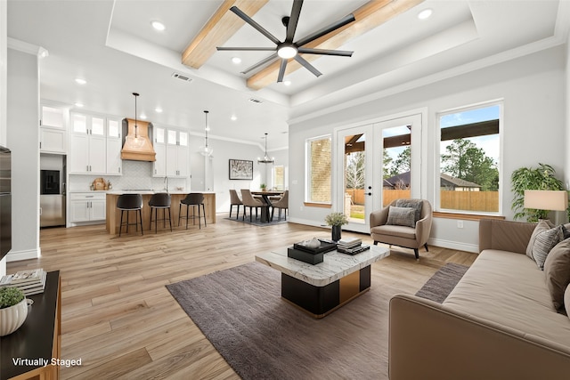 living room with a raised ceiling, ceiling fan, light hardwood / wood-style flooring, french doors, and ornamental molding