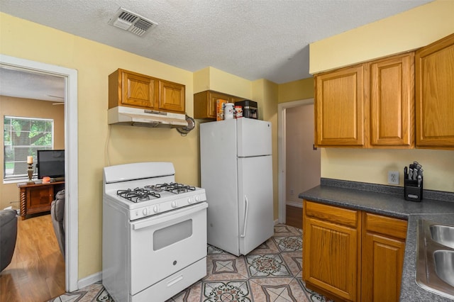 kitchen with white appliances, under cabinet range hood, visible vents, and brown cabinetry