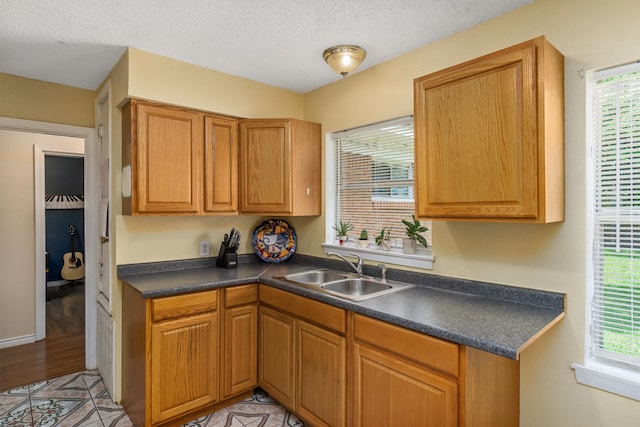 kitchen with dark countertops, a textured ceiling, brown cabinetry, and a sink