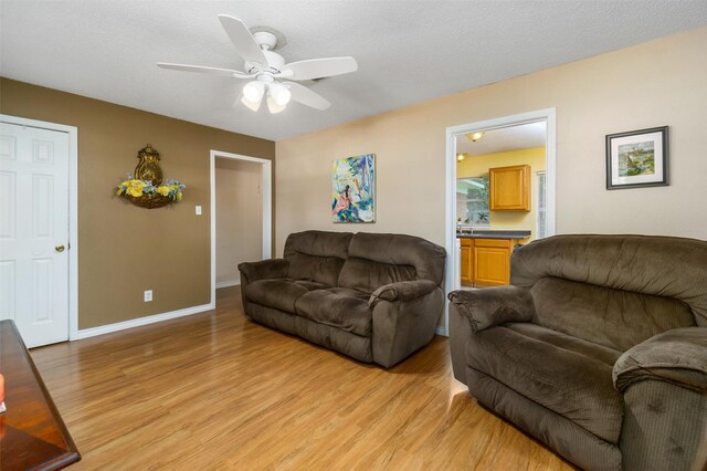 living area with light wood-type flooring, ceiling fan, a textured ceiling, and baseboards