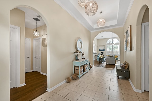 foyer with a notable chandelier, light hardwood / wood-style flooring, ornamental molding, and a tray ceiling