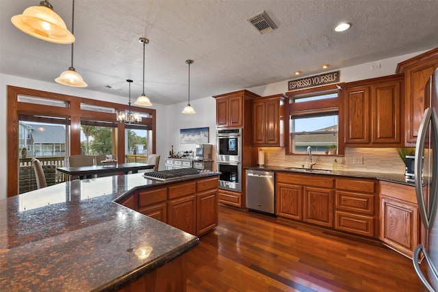 kitchen with sink, dark stone countertops, hanging light fixtures, backsplash, and stainless steel appliances