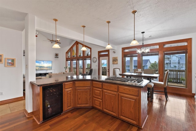 kitchen with dark hardwood / wood-style floors, decorative light fixtures, stainless steel gas stovetop, beverage cooler, and a textured ceiling