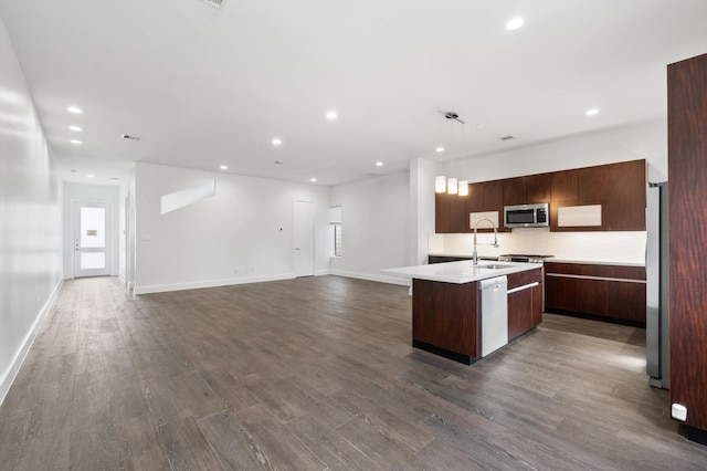 kitchen featuring sink, an island with sink, decorative light fixtures, dark hardwood / wood-style flooring, and stainless steel appliances