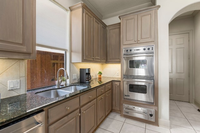 kitchen featuring light tile patterned floors, sink, stainless steel appliances, dark stone countertops, and decorative backsplash