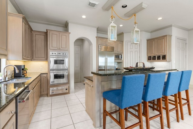 kitchen with sink, decorative light fixtures, built in appliances, dark stone counters, and a kitchen bar