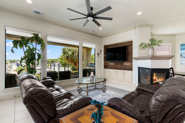 living room featuring crown molding, light tile patterned flooring, a tiled fireplace, and ceiling fan