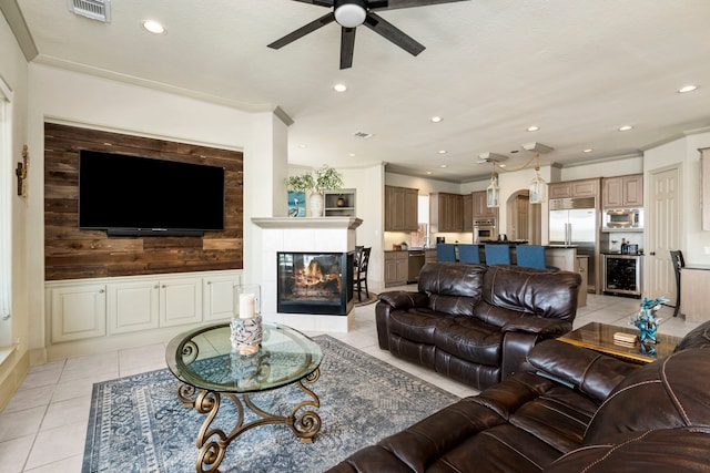 living room featuring a tile fireplace, wood walls, light tile patterned floors, ornamental molding, and ceiling fan