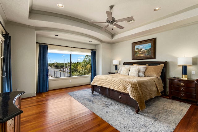 bedroom with wood-type flooring, a raised ceiling, and ceiling fan