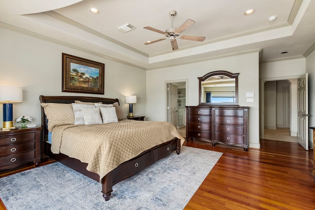 bedroom with a raised ceiling, dark hardwood / wood-style floors, ceiling fan, and ensuite bathroom