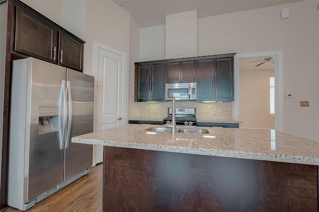 kitchen featuring dark brown cabinetry, stainless steel appliances, light stone counters, light hardwood / wood-style flooring, and backsplash