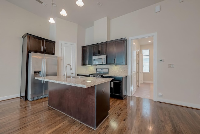 kitchen featuring pendant lighting, a kitchen island with sink, sink, appliances with stainless steel finishes, and dark brown cabinetry