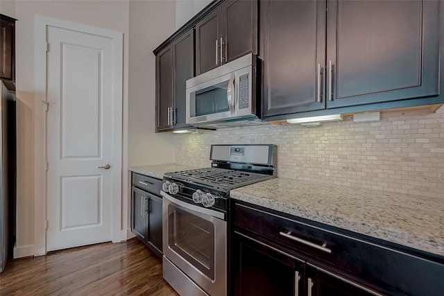 kitchen featuring backsplash, dark wood-type flooring, light stone counters, dark brown cabinetry, and stainless steel appliances