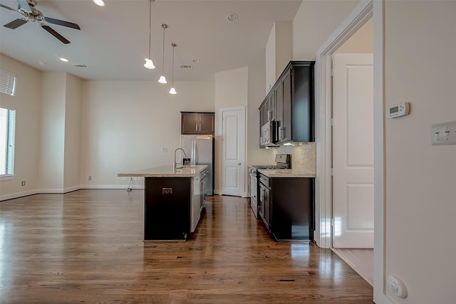 kitchen with stainless steel appliances, light stone counters, decorative light fixtures, decorative backsplash, and a center island with sink