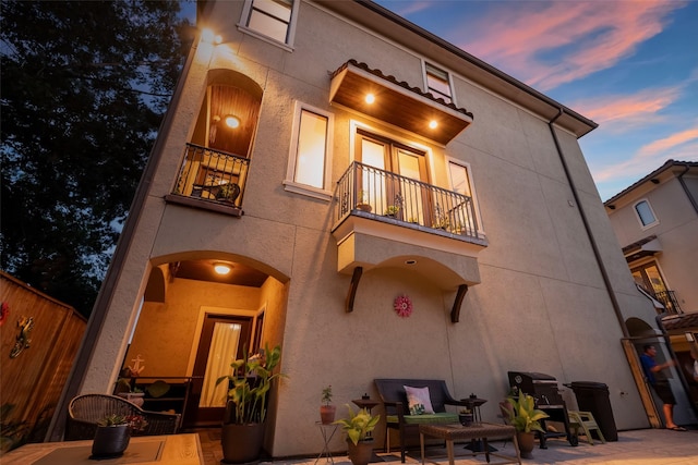 back house at dusk featuring a balcony and a patio area