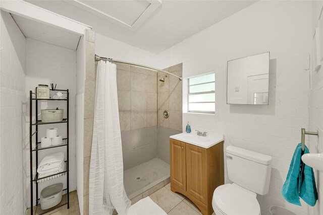 bathroom with vanity, tile patterned floors, a shower with shower curtain, tile walls, and toilet