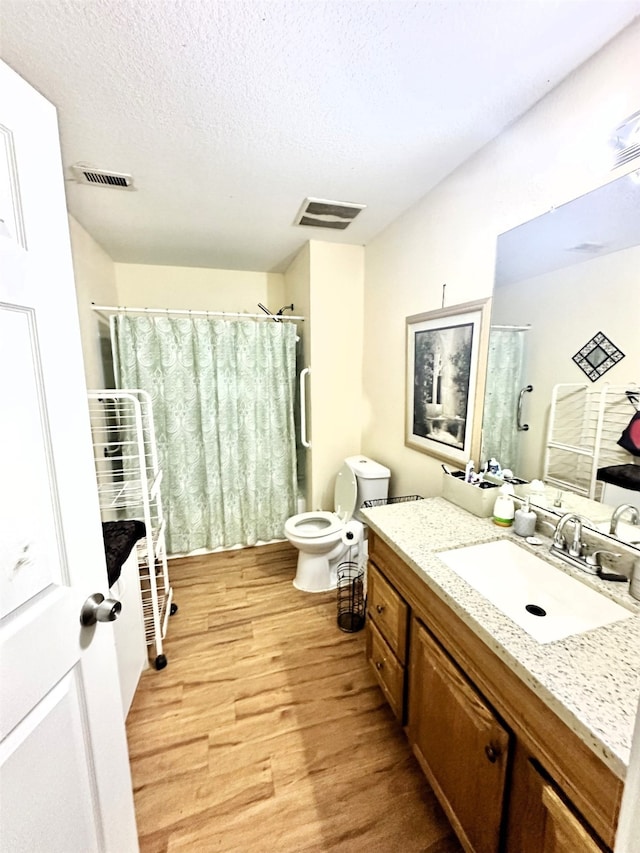 bathroom with a textured ceiling, vanity, toilet, walk in shower, and hardwood / wood-style flooring