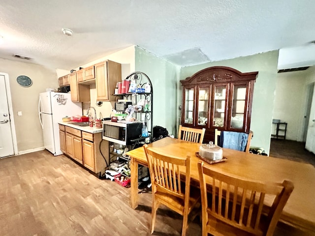 dining area with sink, light wood-type flooring, and a textured ceiling