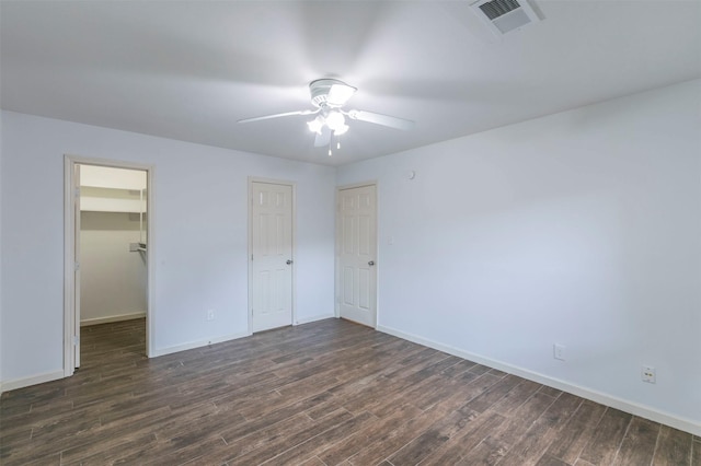 unfurnished bedroom with a closet, a walk in closet, ceiling fan, and dark hardwood / wood-style flooring