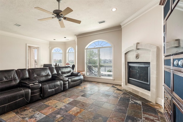 living room with ceiling fan, a textured ceiling, a fireplace, and crown molding