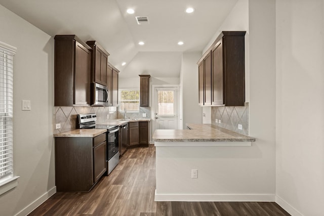 kitchen with tasteful backsplash, appliances with stainless steel finishes, dark wood-type flooring, and kitchen peninsula