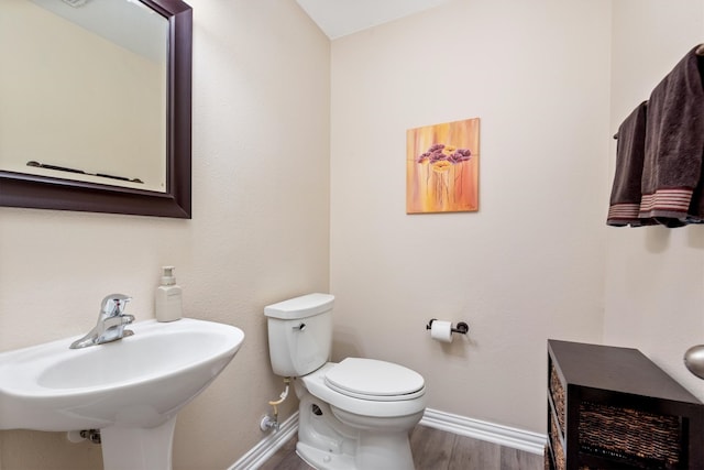 half bath featuring a sink, baseboards, toilet, and wood finished floors