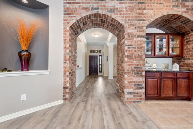 hallway featuring baseboards, brick wall, arched walkways, ornamental molding, and light wood-style floors