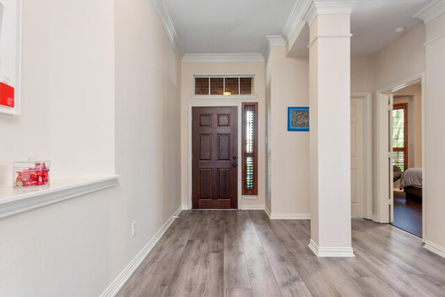 foyer entrance featuring crown molding, decorative columns, wood finished floors, and baseboards