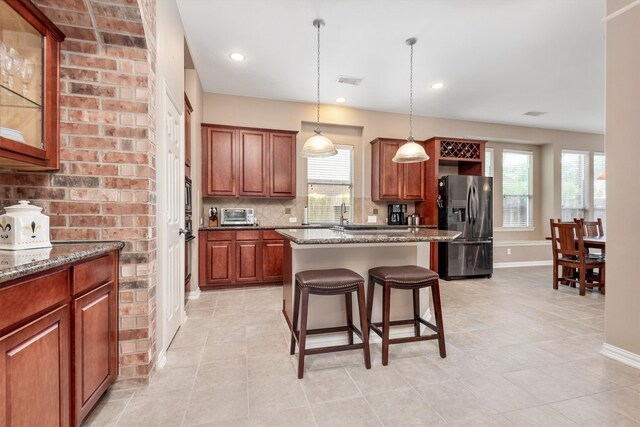 kitchen with dark stone countertops, a breakfast bar area, a kitchen island, stainless steel refrigerator with ice dispenser, and tasteful backsplash