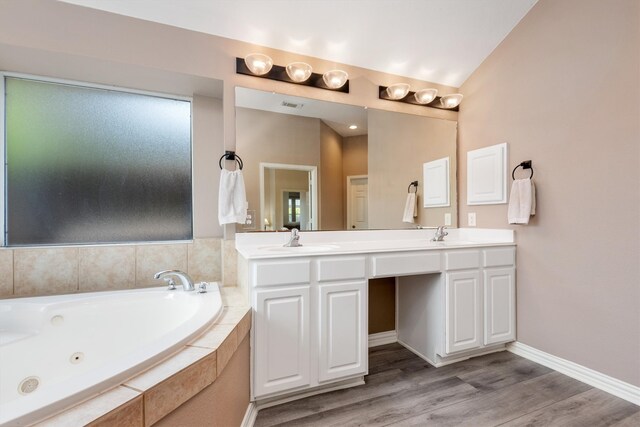 full bathroom with double vanity, a jetted tub, wood finished floors, and a sink