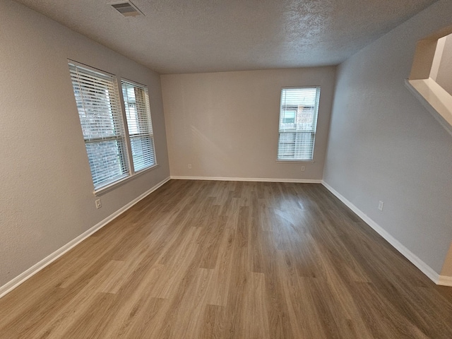 empty room featuring light wood-type flooring, a textured ceiling, and a healthy amount of sunlight