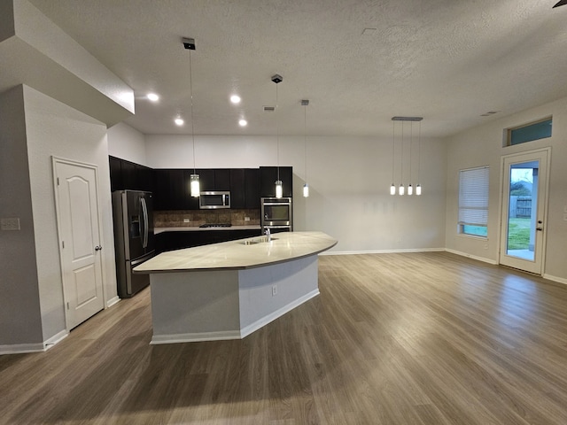 kitchen featuring appliances with stainless steel finishes, backsplash, decorative light fixtures, and a center island with sink