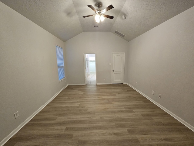 unfurnished room featuring a textured ceiling, vaulted ceiling, ceiling fan, and dark wood-type flooring