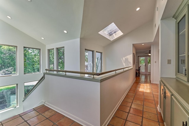 corridor featuring light tile patterned flooring, a healthy amount of sunlight, and lofted ceiling with skylight