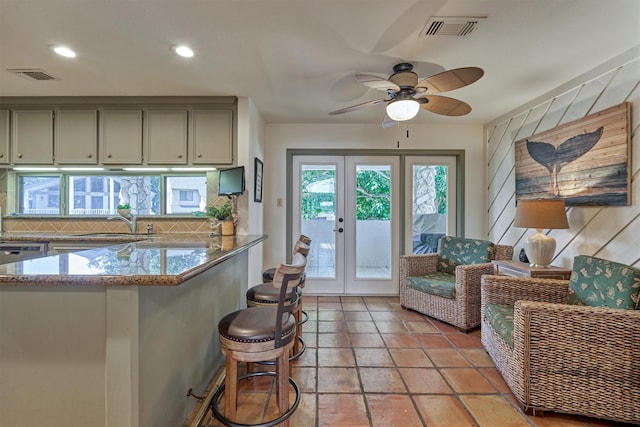 kitchen with french doors, a kitchen breakfast bar, sink, ceiling fan, and light stone countertops