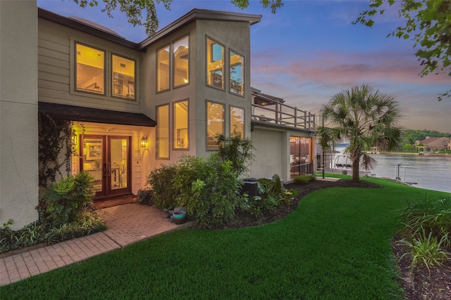 back house at dusk featuring a balcony and a lawn