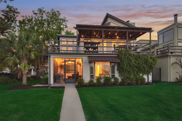 back house at dusk with a balcony and a yard