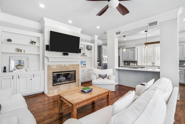 living room with dark wood-type flooring, sink, crown molding, ceiling fan, and a fireplace