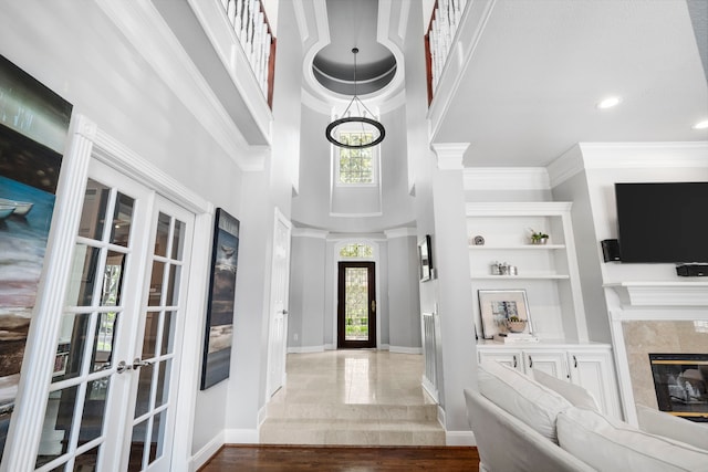 entrance foyer featuring french doors, a towering ceiling, ornamental molding, a fireplace, and dark hardwood / wood-style floors