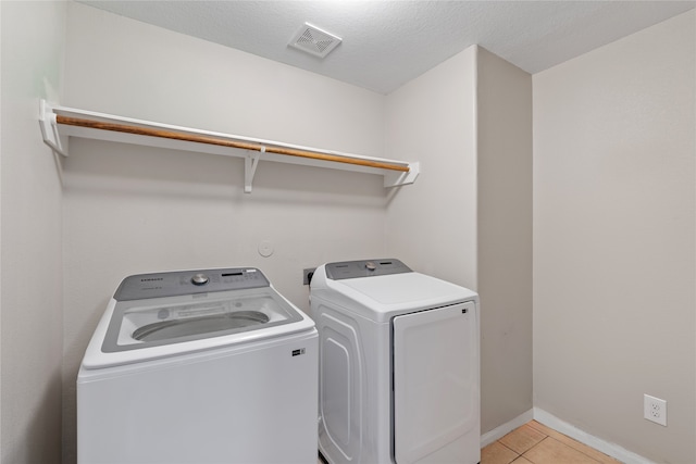 laundry room with light tile patterned flooring, washing machine and dryer, and a textured ceiling