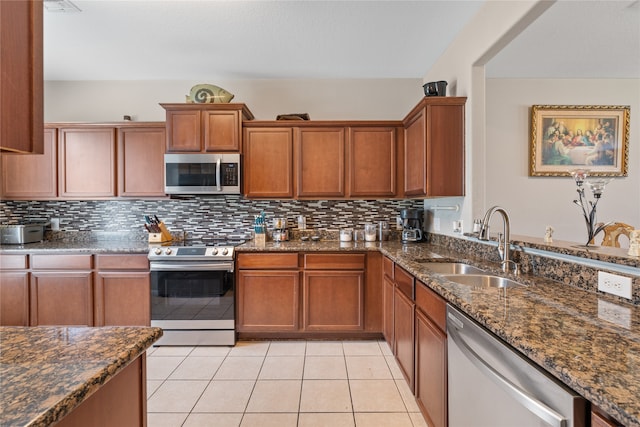 kitchen featuring light tile patterned floors, dark stone counters, backsplash, stainless steel appliances, and sink