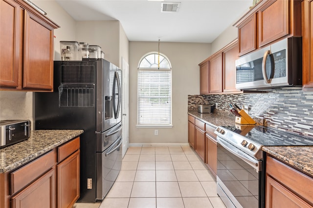 kitchen with dark stone countertops, decorative backsplash, appliances with stainless steel finishes, and light tile patterned flooring